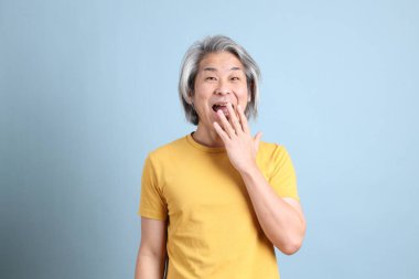 The senior Asian man with yellow t shirt standing on the blue background.