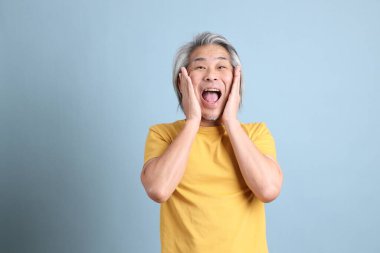 The senior Asian man with yellow t shirt standing on the blue background.
