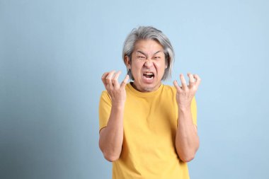 The senior Asian man with yellow t shirt standing on the blue background.
