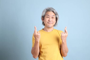 The senior Asian man with yellow t shirt standing on the blue background.