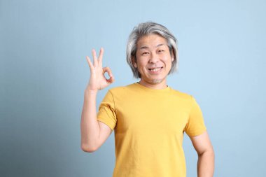 The senior Asian man with yellow t shirt standing on the blue background.