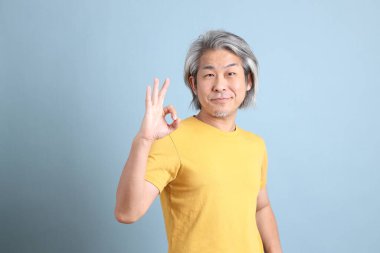 The senior Asian man with yellow t shirt standing on the blue background.