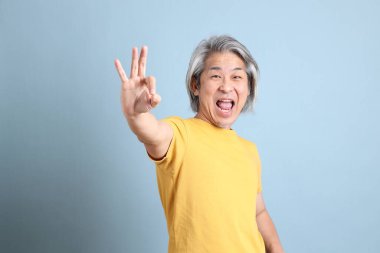 The senior Asian man with yellow t shirt standing on the blue background.