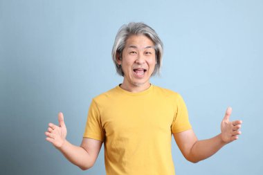 The senior Asian man with yellow t shirt standing on the blue background.