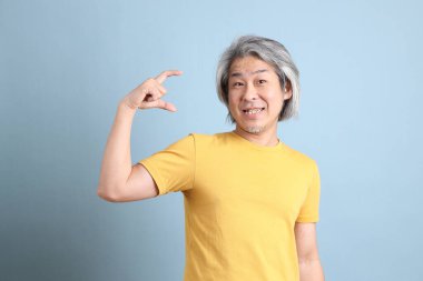 The senior Asian man with yellow t shirt standing on the blue background.