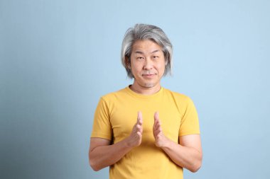 The senior Asian man with yellow t shirt standing on the blue background.