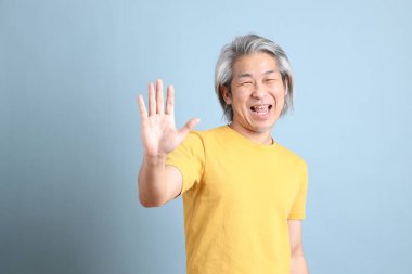 The senior Asian man with yellow t shirt standing on the blue background.