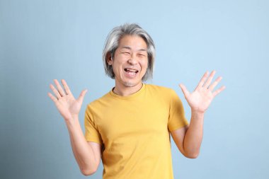 The senior Asian man with yellow t shirt standing on the blue background.