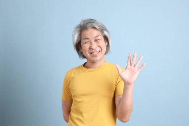 The senior Asian man with yellow t shirt standing on the blue background.