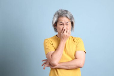 The senior Asian man with yellow t shirt standing on the blue background.