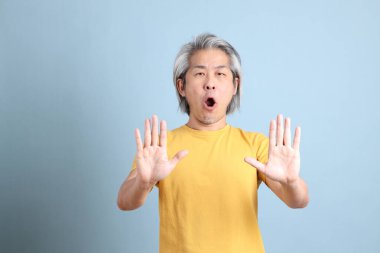 The senior Asian man with yellow t shirt standing on the blue background.