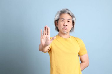 The senior Asian man with yellow t shirt standing on the blue background.