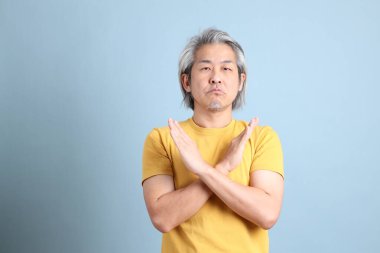 The senior Asian man with yellow t shirt standing on the blue background.