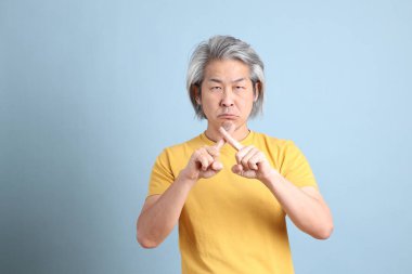 The senior Asian man with yellow t shirt standing on the blue background.