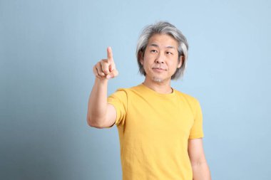 The senior Asian man with yellow t shirt standing on the blue background.