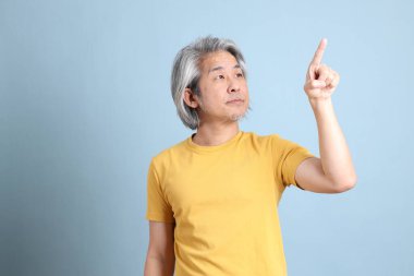 The senior Asian man with yellow t shirt standing on the blue background.