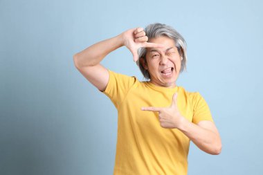 The senior Asian man with yellow t shirt standing on the blue background.