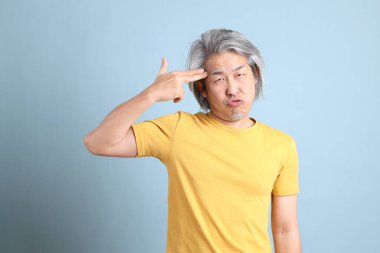 The senior Asian man with yellow t shirt standing on the blue background.