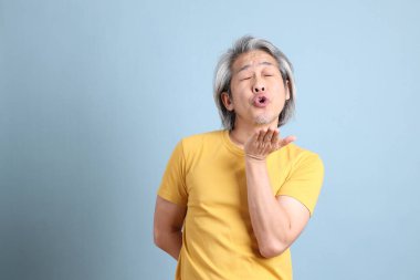 The senior Asian man with yellow t shirt standing on the blue background.