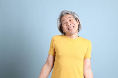 The senior Asian man with yellow t shirt standing on the blue background.