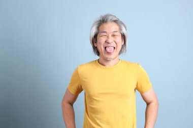 The senior Asian man with yellow t shirt standing on the blue background.
