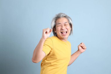 The senior Asian man with yellow t shirt standing on the blue background.