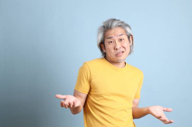 The senior Asian man with yellow t shirt standing on the blue background.