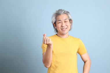 The senior Asian man with yellow t shirt standing on the blue background.