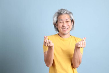 The senior Asian man with yellow t shirt standing on the blue background.