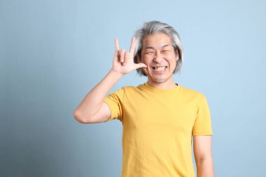 The senior Asian man with yellow t shirt standing on the blue background.