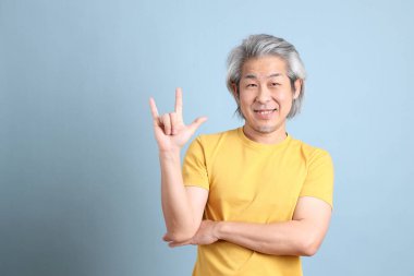 The senior Asian man with yellow t shirt standing on the blue background.