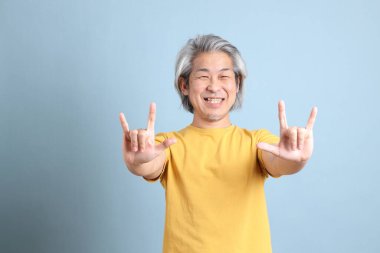 The senior Asian man with yellow t shirt standing on the blue background.