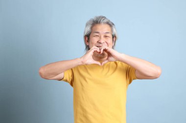 The senior Asian man with yellow t shirt standing on the blue background.
