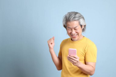 The senior Asian man with yellow t shirt standing on the blue background.