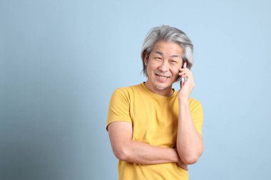 The senior Asian man with yellow t shirt standing on the blue background.