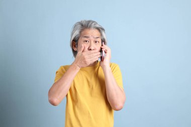 The senior Asian man with yellow t shirt standing on the blue background.