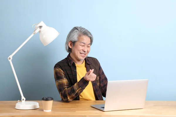 Starszy Azjata Żółtej Koszuli Pracujący Laptopie Niebieskim Tle — Zdjęcie stockowe