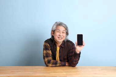 The senior Asian man using smart phone at the working desk with blue background.