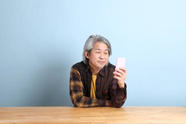 The senior Asian man using smart phone at the working desk with blue background.