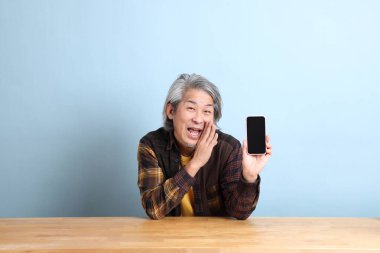The senior Asian man using smart phone at the working desk with blue background.