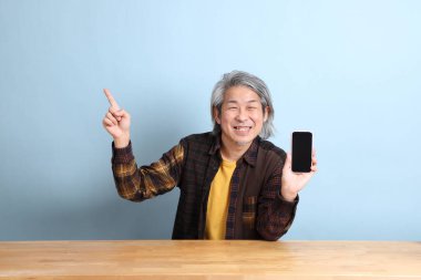 The senior Asian man using smart phone at the working desk with blue background.