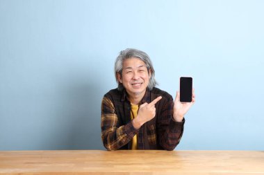 The senior Asian man using smart phone at the working desk with blue background.