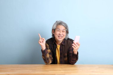 The senior Asian man using smart phone at the working desk with blue background.
