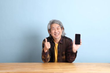 The senior Asian man using smart phone at the working desk with blue background.