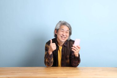 The senior Asian man using smart phone at the working desk with blue background.