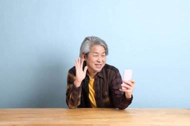 The senior Asian man using smart phone at the working desk with blue background.
