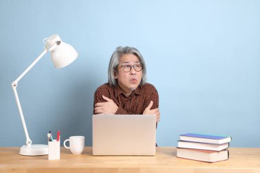 The senior Asian man working on the laptop at the desk with blue background.