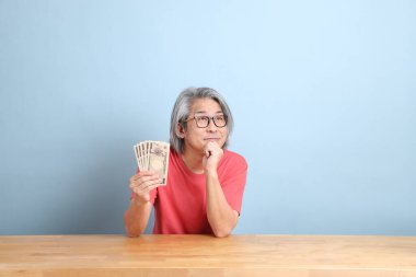 The senior Asian man with colorful shirt sitting at the desk with blue background.