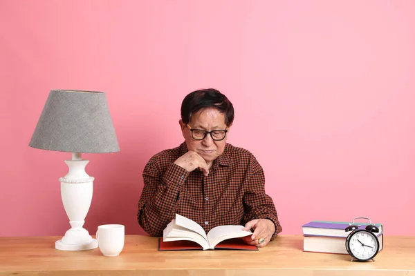 Senior Asian Woman Reading Book Sitting Desk Pink Background — Stockfoto