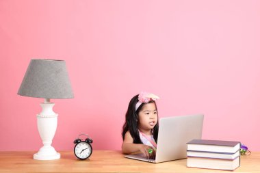 The cute Asian girl learning from internet by laptop with the pink background.